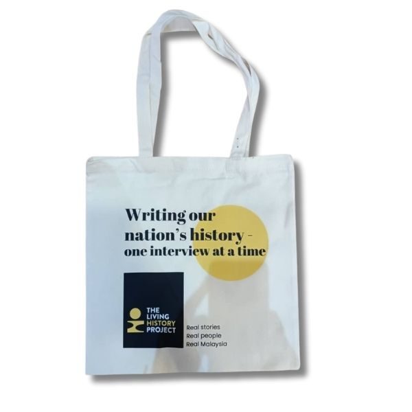 White canvas tote bag with black and yellow graphic design, featuring the slogan 'Writing our nation's history - one interview at a time' and 'The Living History Project' logo with 'Real stories, Real people, Real Malaysia' tagline.